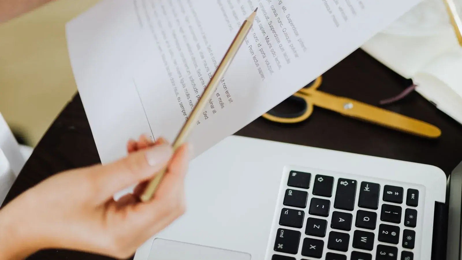 Hand mit Bleistift prüft ein Vertragsdokument neben einem aufgeklappten Laptop — Sinnbild für die Kalkulation von Webdesign-Preisen